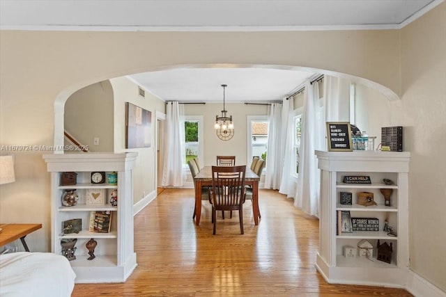 dining area featuring ornamental molding, arched walkways, a chandelier, and light wood finished floors