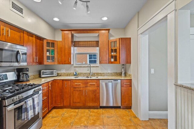 kitchen with stainless steel appliances, light stone countertops, and sink