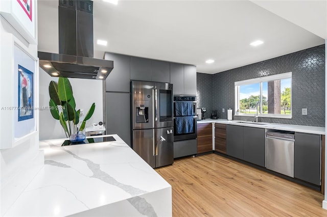 kitchen with decorative backsplash, wall chimney exhaust hood, stainless steel appliances, sink, and light wood-type flooring