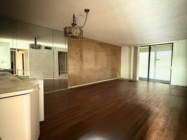 unfurnished living room with an inviting chandelier, a textured ceiling, and dark hardwood / wood-style flooring