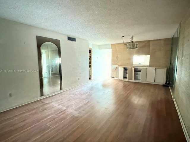 empty room featuring a textured ceiling, an inviting chandelier, and dark hardwood / wood-style flooring