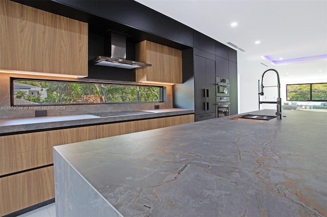 kitchen featuring sink, wall chimney exhaust hood, black electric cooktop, a kitchen island, and stainless steel double oven