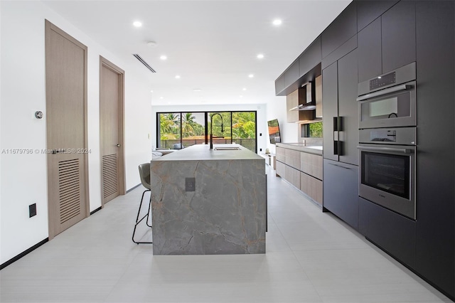 kitchen with sink, stainless steel double oven, a kitchen bar, a kitchen island with sink, and light tile patterned floors