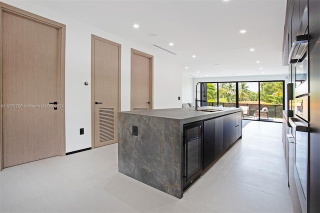 kitchen with light brown cabinets, a center island with sink, and beverage cooler