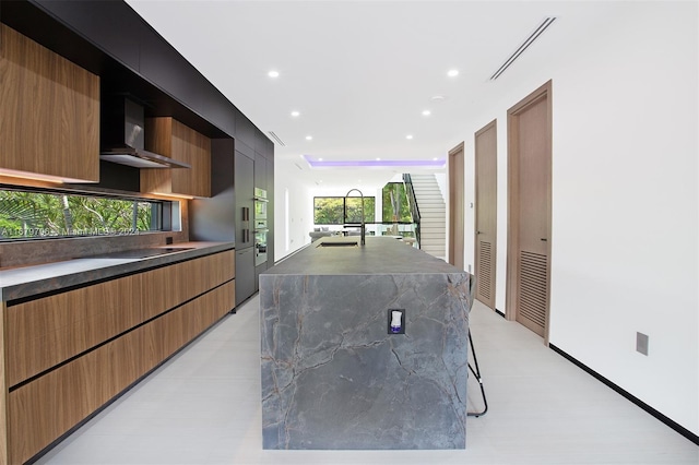 kitchen featuring a kitchen island with sink, black electric stovetop, and wall chimney range hood