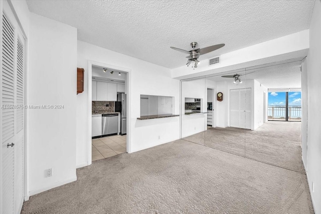 unfurnished living room with ceiling fan, light carpet, and a textured ceiling