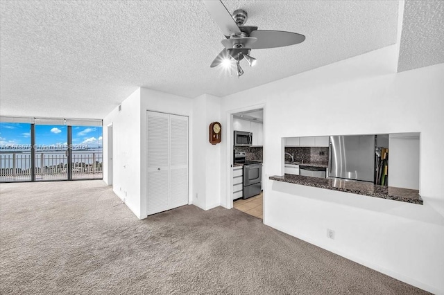 unfurnished living room featuring floor to ceiling windows, a textured ceiling, light colored carpet, and ceiling fan