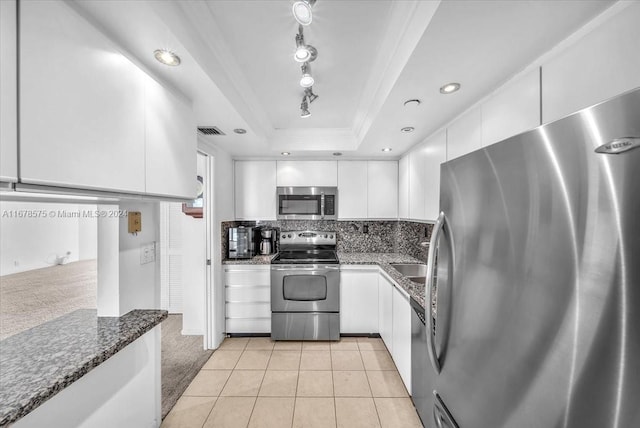 kitchen featuring white cabinetry, dark stone counters, a tray ceiling, light tile patterned floors, and appliances with stainless steel finishes