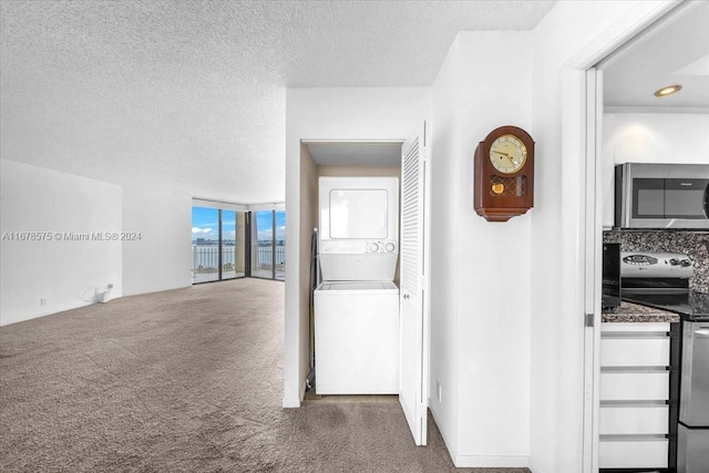 hall featuring a textured ceiling, dark carpet, and stacked washer / dryer