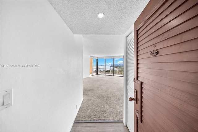 hall featuring floor to ceiling windows, light hardwood / wood-style floors, and a textured ceiling