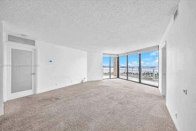 empty room featuring carpet flooring, a textured ceiling, a water view, and expansive windows