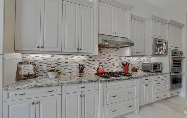 kitchen with light stone countertops, white cabinets, appliances with stainless steel finishes, and tasteful backsplash