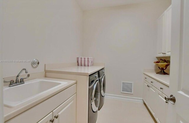 clothes washing area with sink, washing machine and clothes dryer, light tile patterned floors, and cabinets