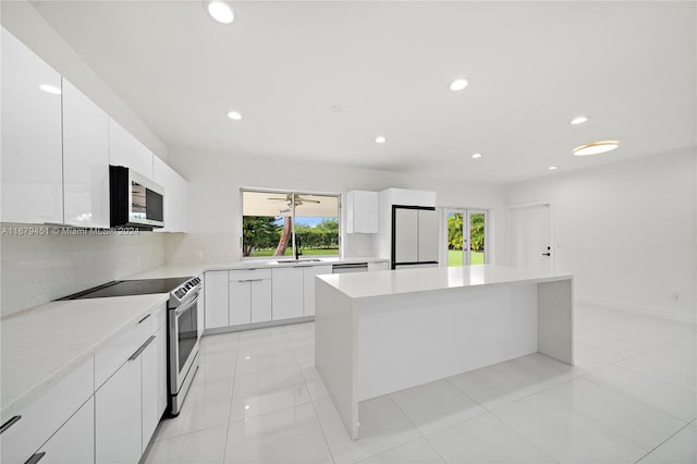 kitchen with appliances with stainless steel finishes, sink, a kitchen island, backsplash, and white cabinets