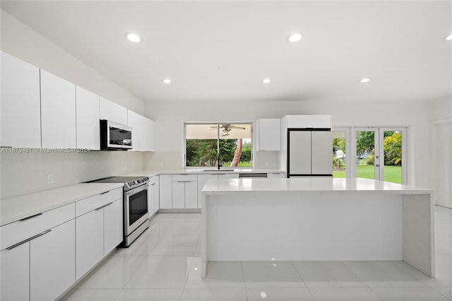 kitchen with white cabinets, light tile patterned flooring, stainless steel appliances, sink, and a center island