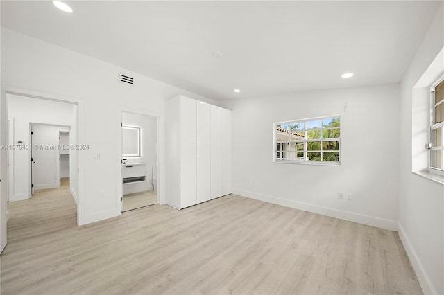 unfurnished bedroom with a closet, ensuite bath, and light wood-type flooring