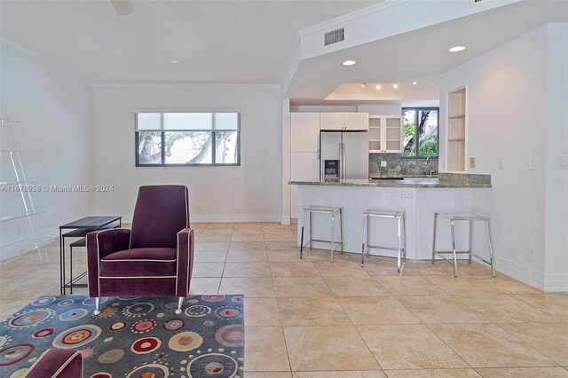 kitchen featuring kitchen peninsula, stainless steel fridge, a kitchen bar, white cabinets, and tasteful backsplash