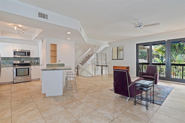 kitchen with decorative backsplash, crown molding, white cabinets, a kitchen bar, and appliances with stainless steel finishes