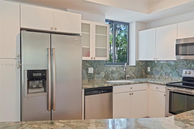 kitchen with tasteful backsplash, appliances with stainless steel finishes, sink, white cabinetry, and light stone counters