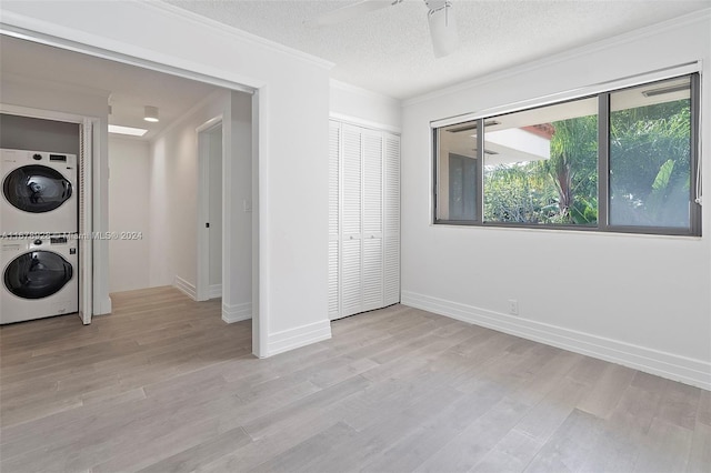 unfurnished bedroom featuring a textured ceiling, a closet, ceiling fan, light hardwood / wood-style floors, and stacked washer and dryer