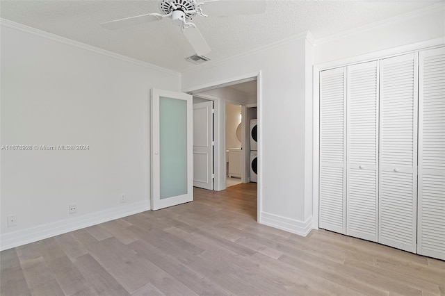 unfurnished bedroom featuring stacked washer and clothes dryer, a closet, a textured ceiling, light hardwood / wood-style floors, and ceiling fan