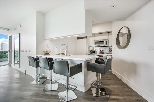 kitchen featuring white cabinets, decorative backsplash, dark hardwood / wood-style flooring, a breakfast bar, and paneled built in refrigerator