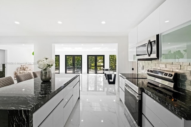 kitchen with appliances with stainless steel finishes, dark stone counters, white cabinetry, and a spacious island