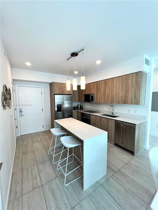 kitchen with a kitchen island, appliances with stainless steel finishes, a breakfast bar, pendant lighting, and sink