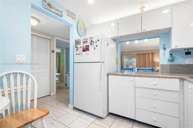 kitchen with white cabinets, a textured ceiling, light tile patterned floors, and white refrigerator