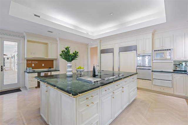 kitchen featuring built in appliances, white cabinetry, light parquet flooring, a raised ceiling, and a center island