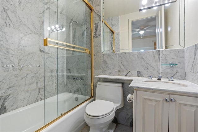 full bathroom with toilet, tile walls, bath / shower combo with glass door, vanity, and ceiling fan