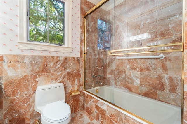 bathroom featuring toilet, bath / shower combo with glass door, and tile walls