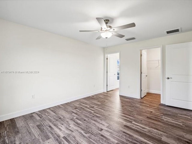 unfurnished bedroom featuring a spacious closet, dark wood-type flooring, a closet, and ceiling fan