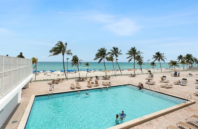 view of swimming pool featuring a view of the beach, a water view, and a patio area