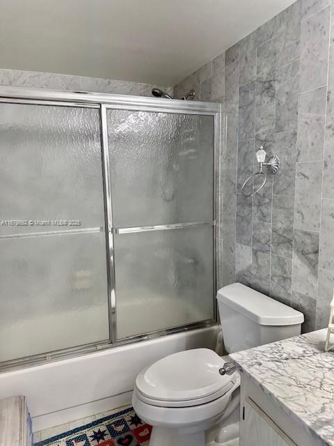 full bathroom with vanity, toilet, tile walls, and bath / shower combo with glass door