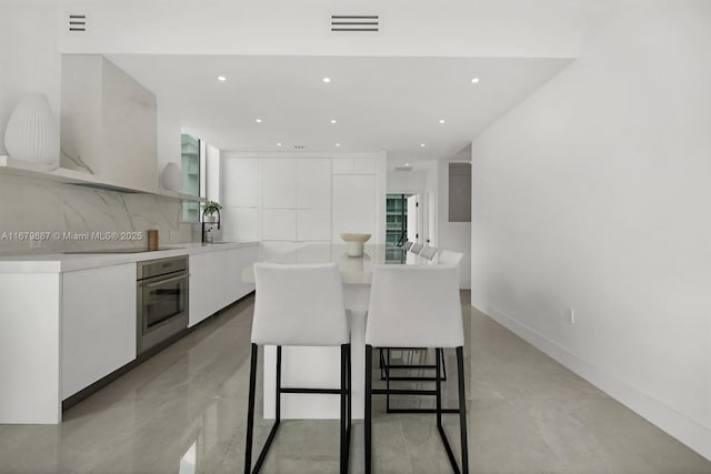 kitchen featuring white cabinetry, stainless steel oven, light countertops, backsplash, and modern cabinets