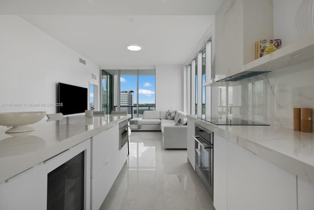 kitchen with marble finish floor, stainless steel appliances, white cabinets, a wall of windows, and beverage cooler