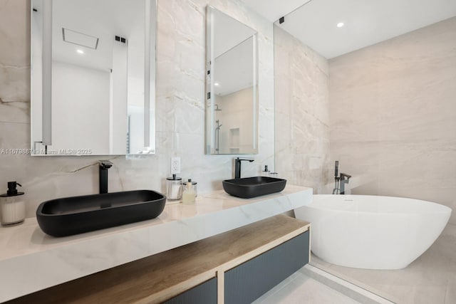 full bathroom with double vanity, a freestanding tub, a sink, and tile walls