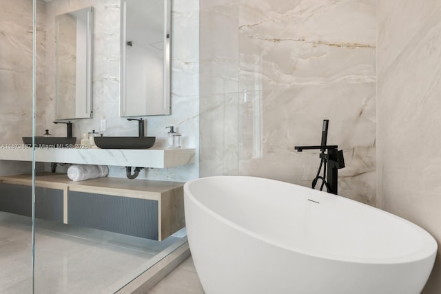 full bath featuring tile walls, double vanity, a freestanding bath, a sink, and tile patterned floors