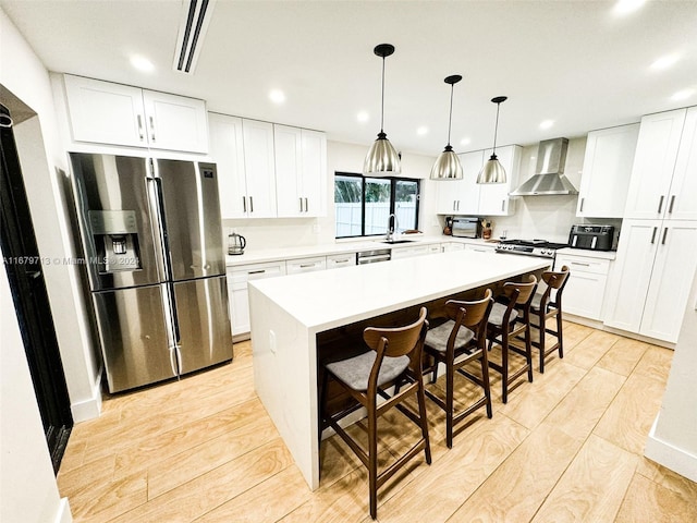 kitchen featuring a center island, wall chimney range hood, a kitchen breakfast bar, light hardwood / wood-style floors, and appliances with stainless steel finishes