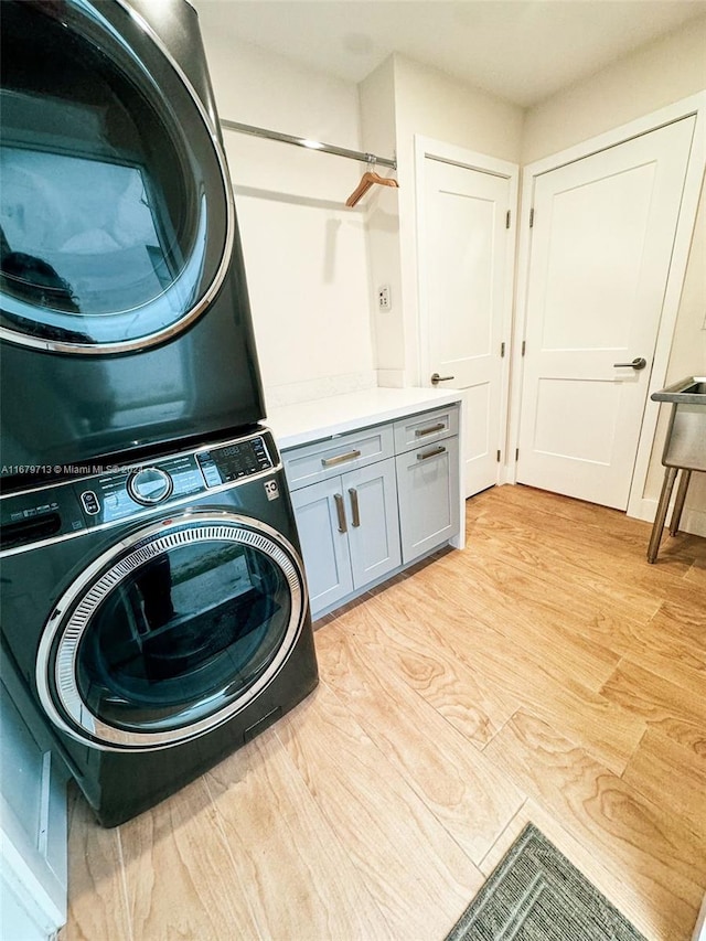 clothes washing area featuring cabinets, light wood-type flooring, and stacked washing maching and dryer