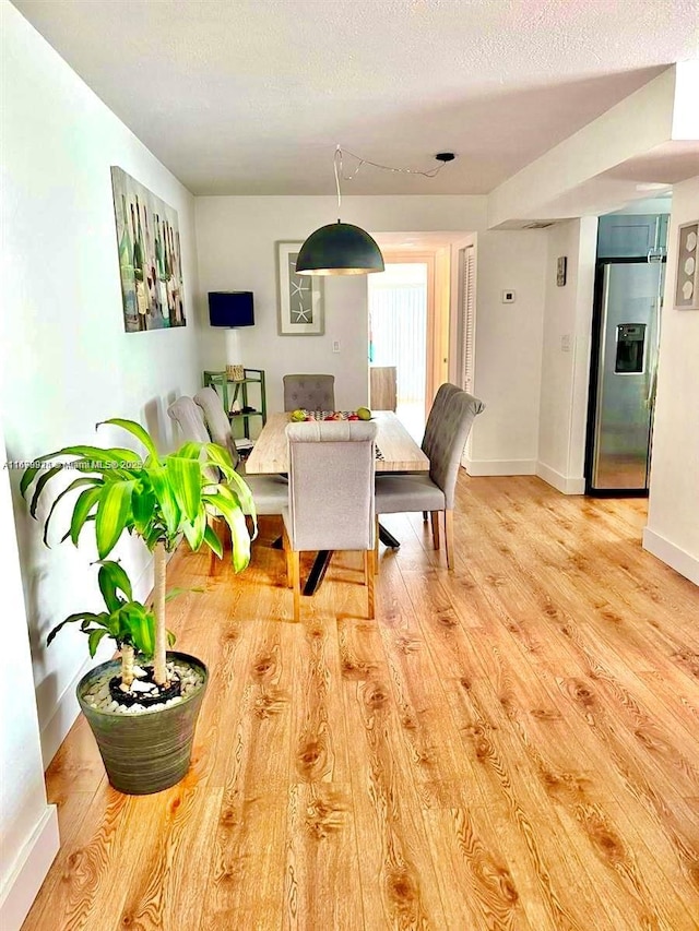 dining area with baseboards, light wood-style flooring, and a textured ceiling