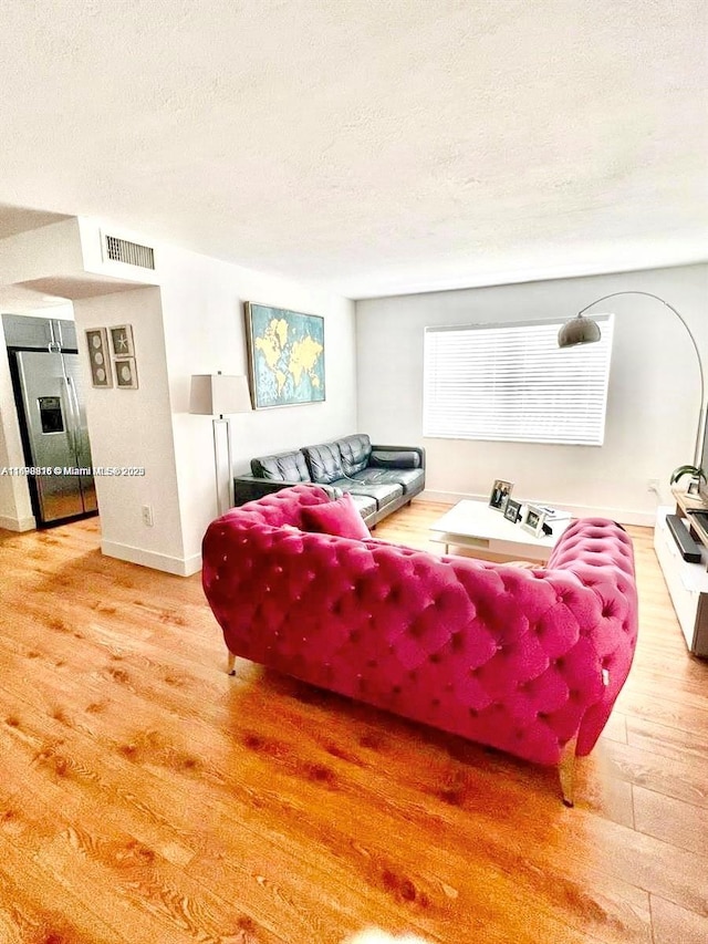 living room featuring baseboards, visible vents, a textured ceiling, and light wood finished floors