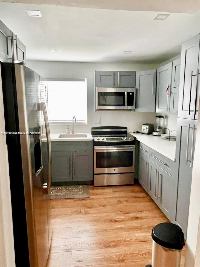 kitchen with gray cabinets, light countertops, light wood-style flooring, appliances with stainless steel finishes, and a sink