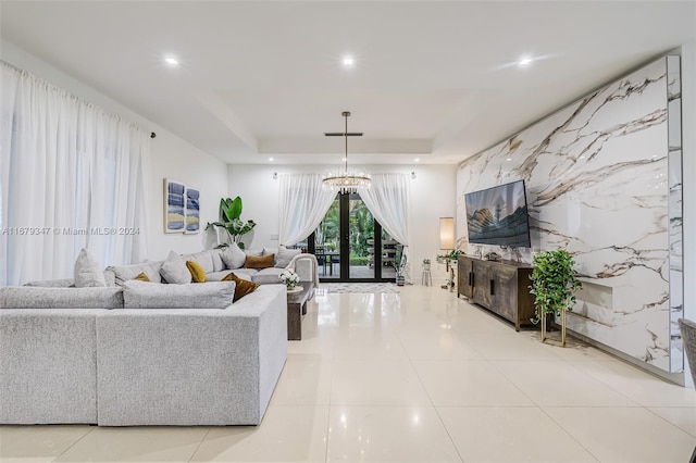 living room with a notable chandelier, a tray ceiling, and light tile patterned flooring