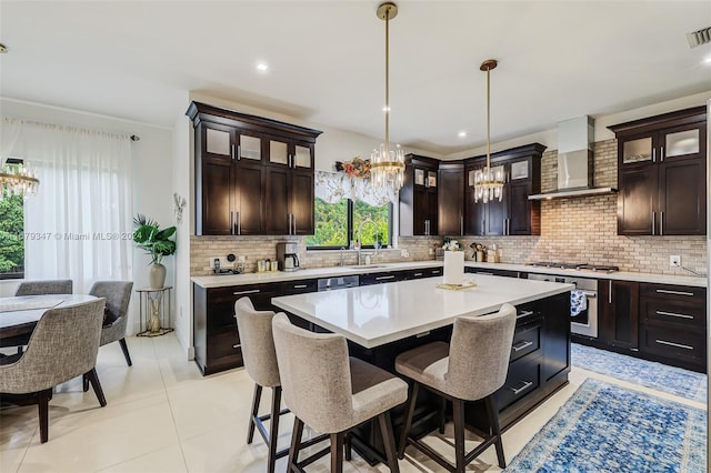 kitchen featuring wall chimney exhaust hood, a center island, dark brown cabinets, and pendant lighting