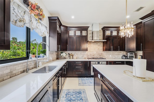 kitchen featuring wall chimney range hood, sink, hanging light fixtures, stainless steel appliances, and decorative backsplash