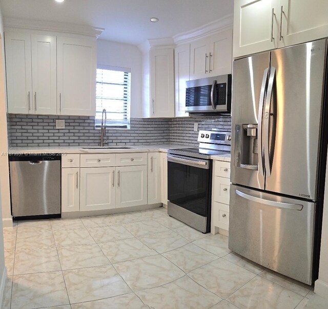 kitchen with decorative backsplash, white cabinets, appliances with stainless steel finishes, crown molding, and sink