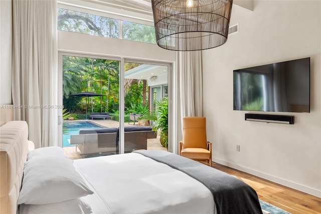 bedroom with a towering ceiling, wood-type flooring, multiple windows, and access to exterior