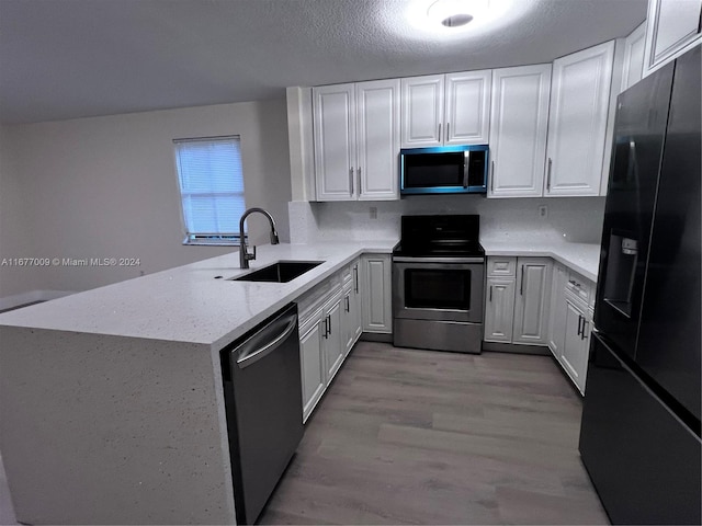 kitchen featuring kitchen peninsula, appliances with stainless steel finishes, white cabinetry, light hardwood / wood-style flooring, and sink